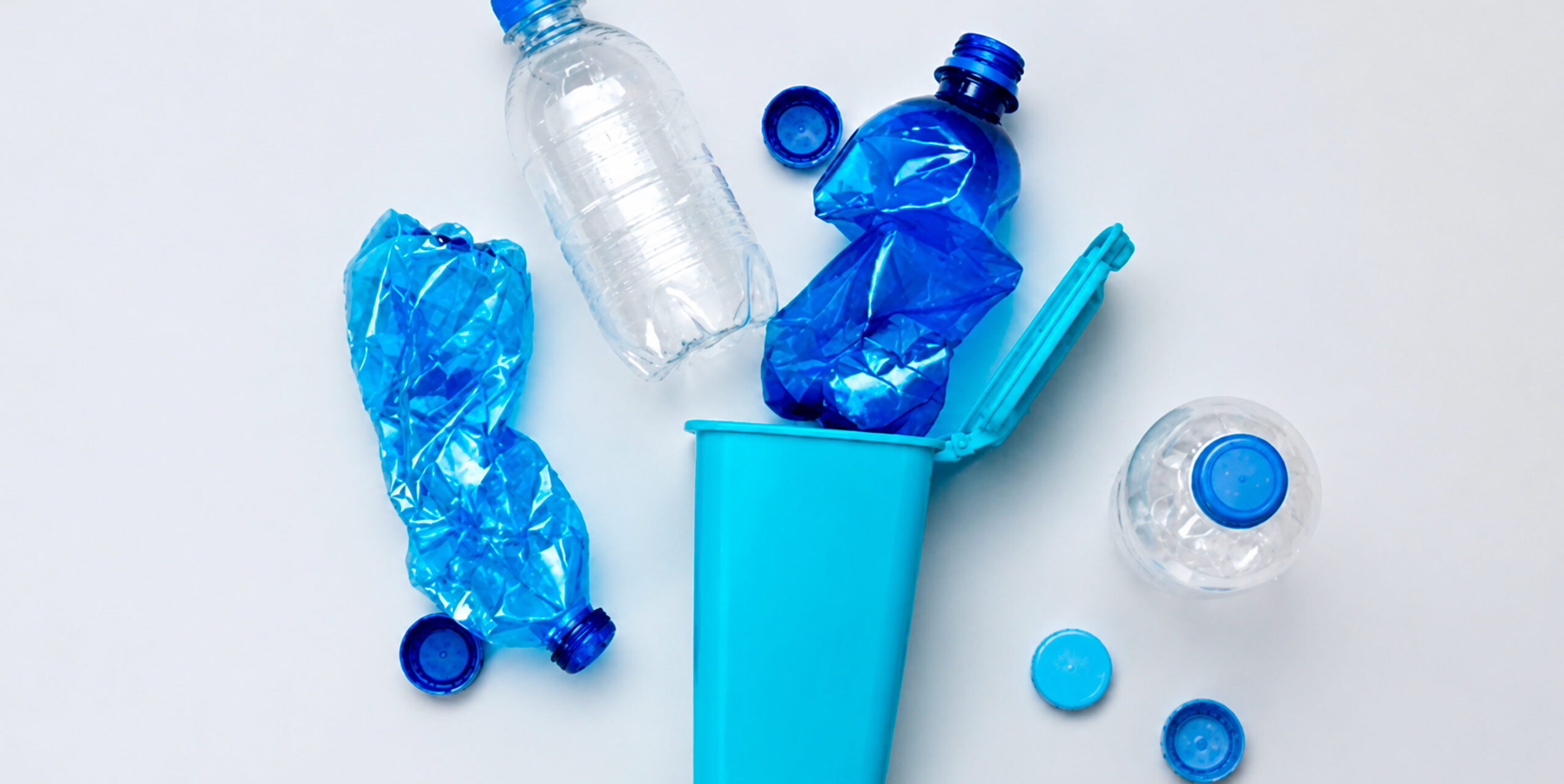 sammenklemte plastikflasker og skruelåg samlet ved en lille affaldsspand