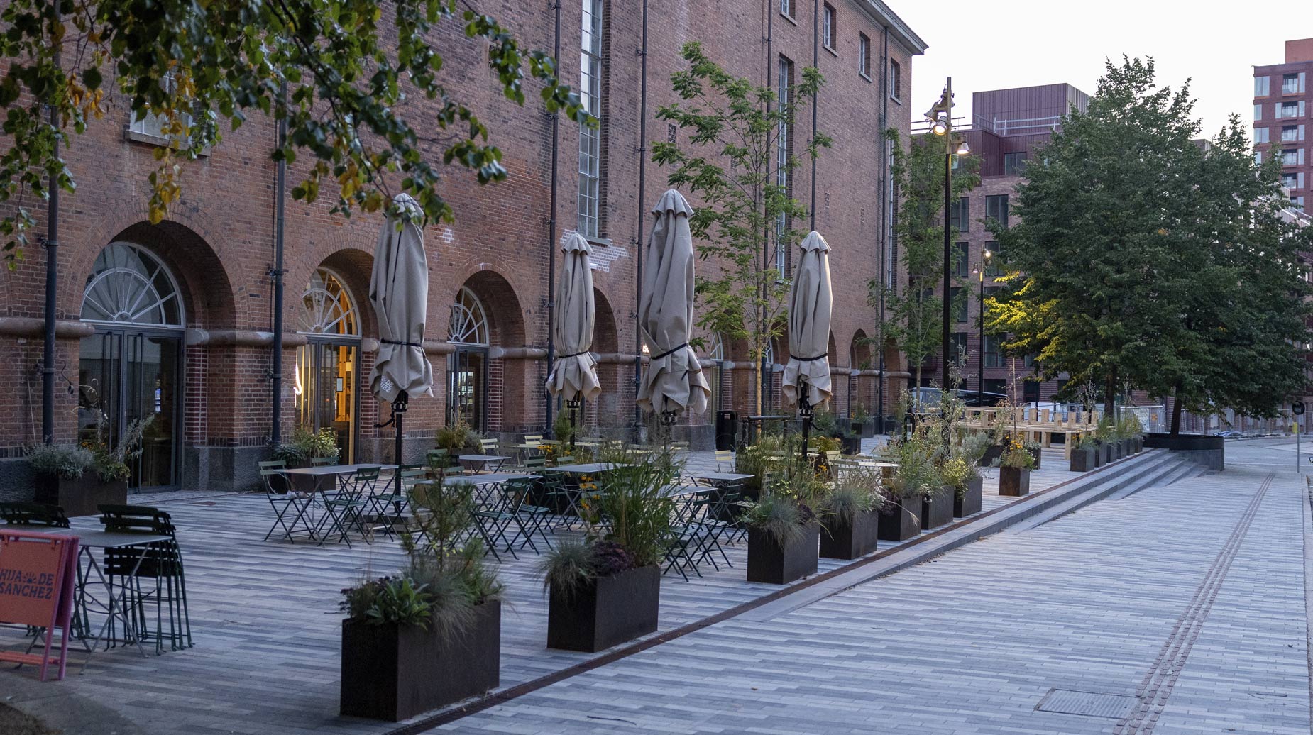 Beplantede plantekasser med græsser og stauder langs belagt gadeareal foran ombygget pakhus.