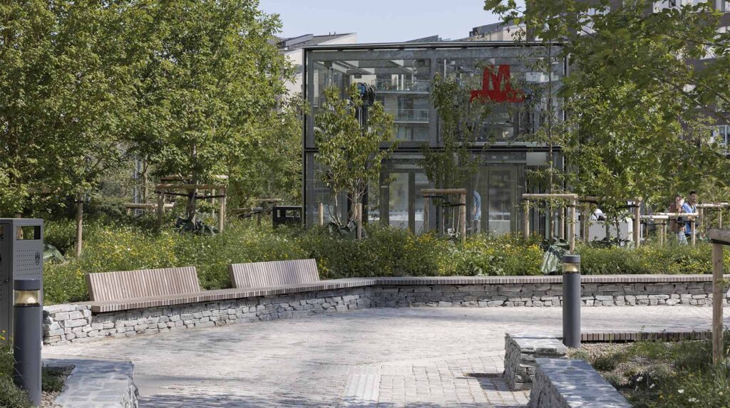 Anlagt byrum med træbænke, stensat mur og beplantning ved metrostation