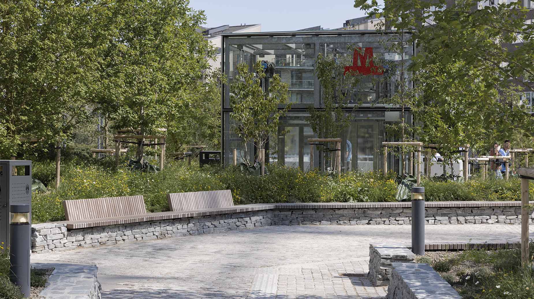 Anlagt byrum med træbænke, stensat mur og beplantning ved metrostation