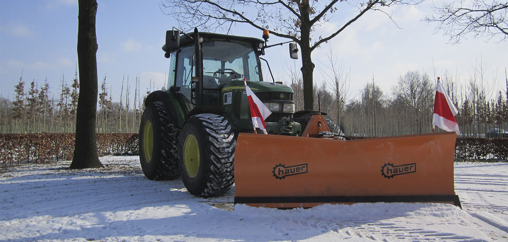 Traktor med monteret sneplov rydder sne på grusvej ved plantageareal.