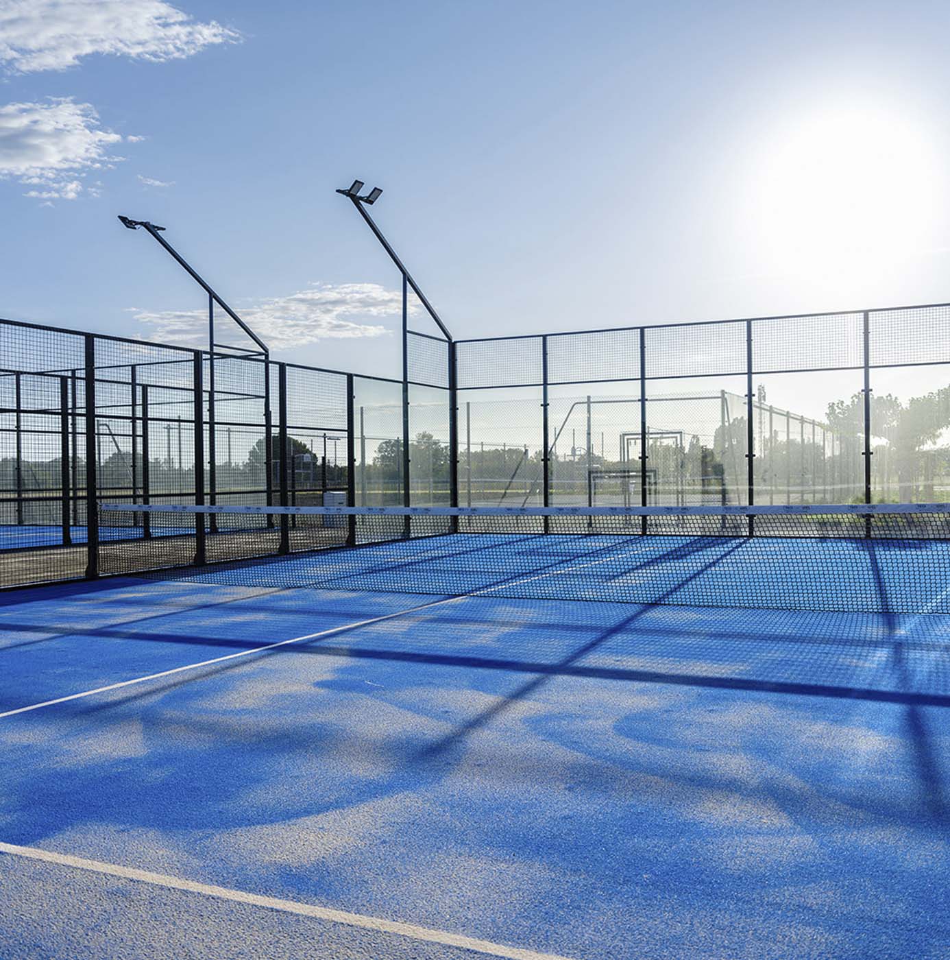 Nyanlagt padelbane med blåt kunstgræsunderlag og glasfiberhegn i klart sollys.