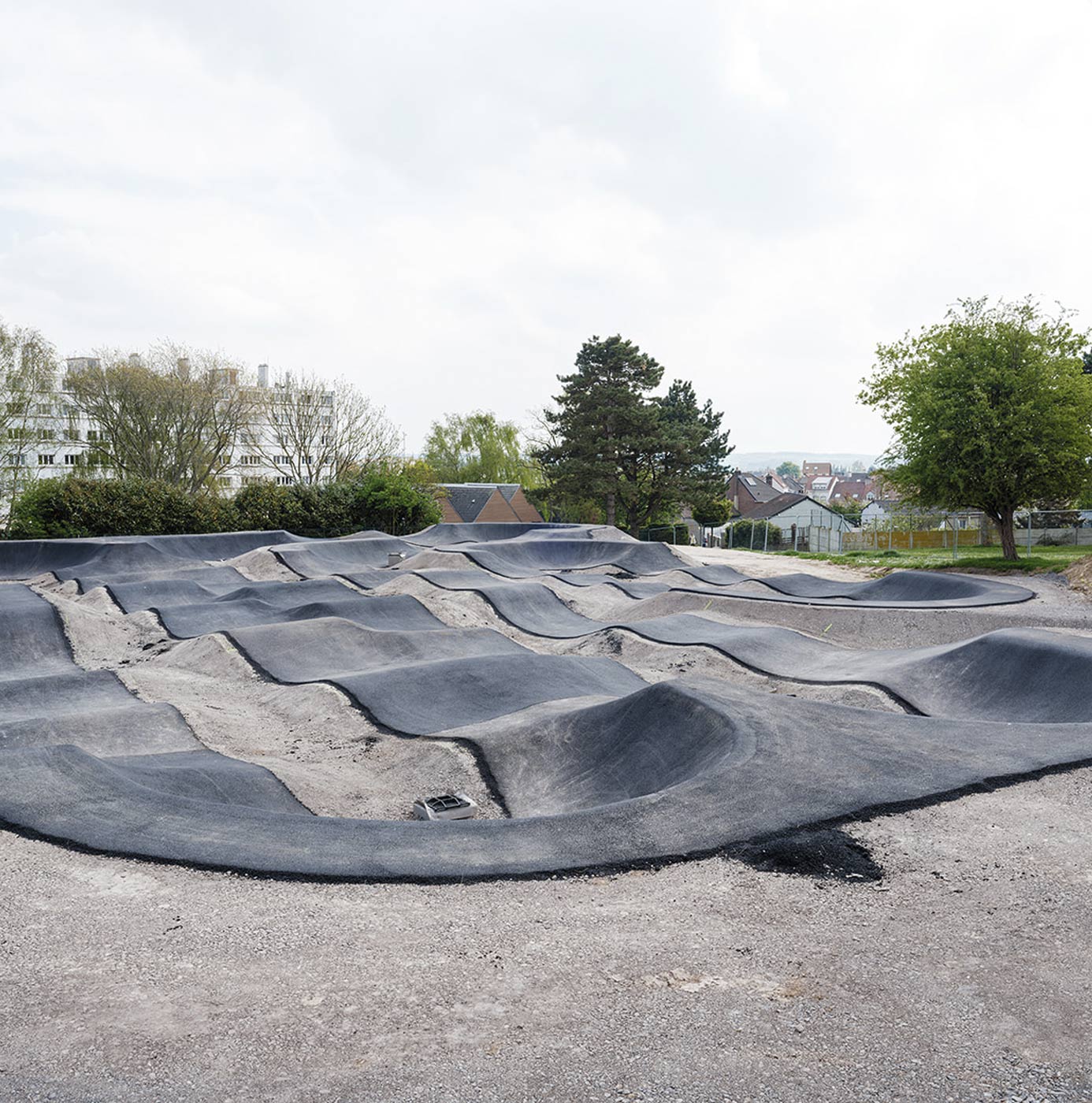 Nyanlagt pumptrack-bane med bølgende asfaltspor i byområde.