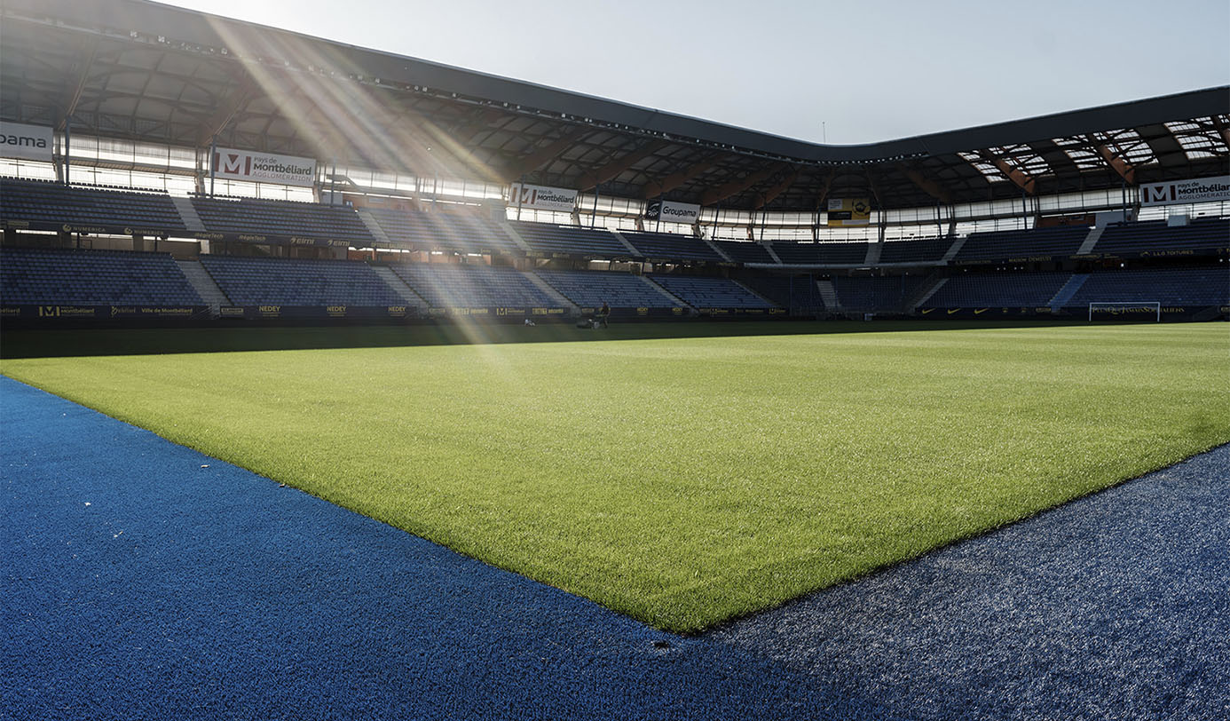 Nyklippet fodboldbane på stadion med tribuner i baggrunden.