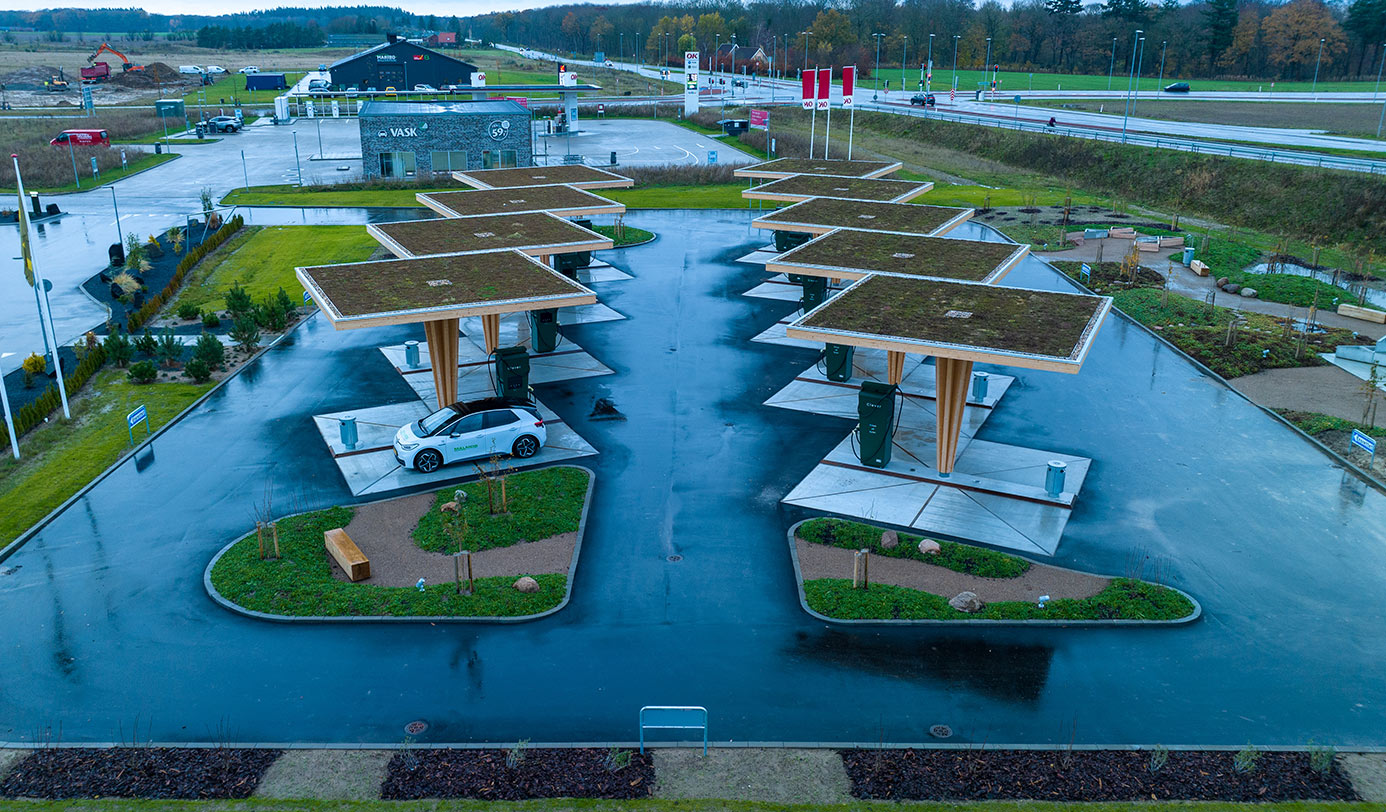 Ladestation for elbiler med grønne sedumtage over ladestandere og beplantede øer med lav vegetation.