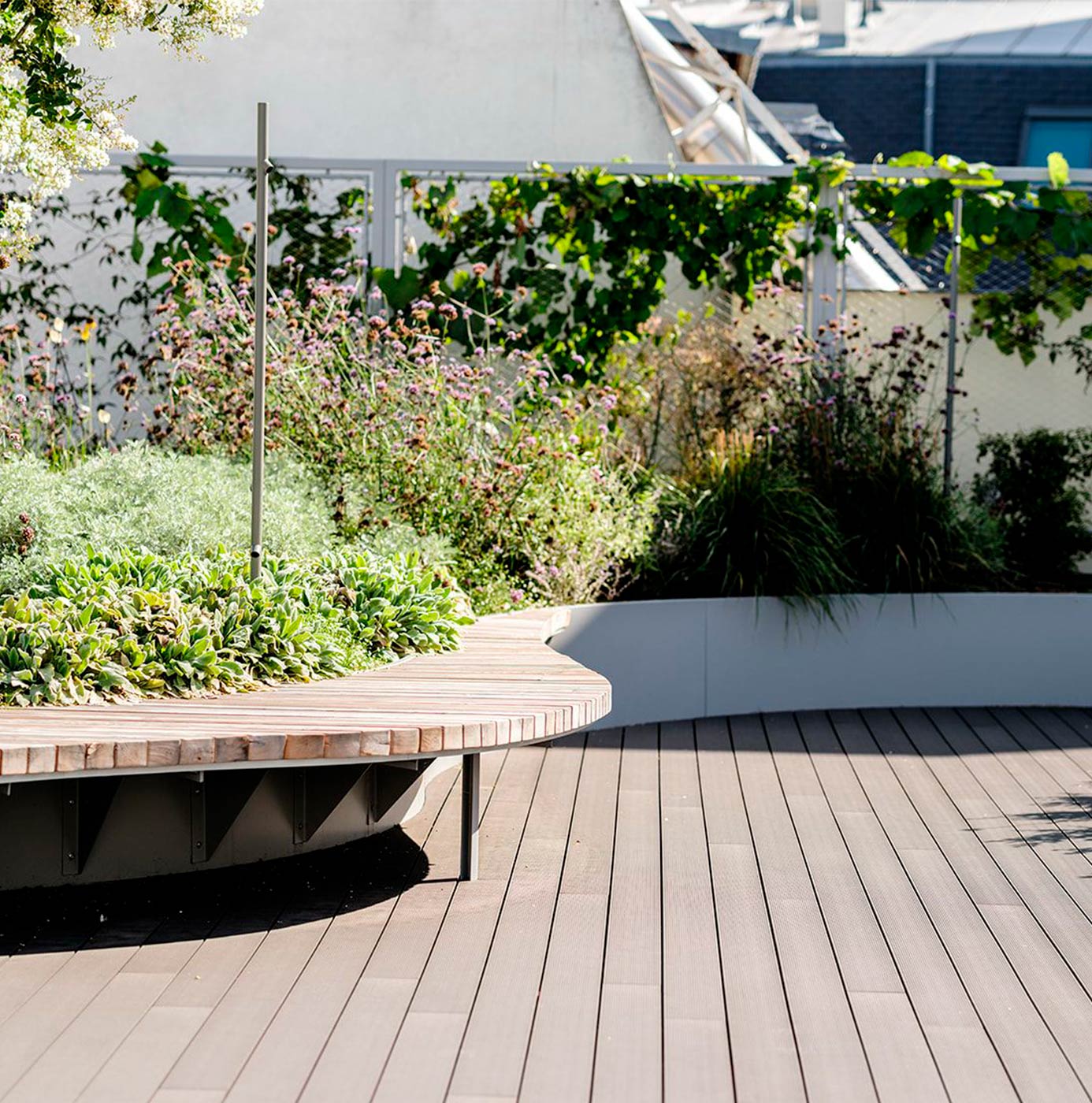 Grønt tag med buet træterrasse og plantebede med stauder og prydgræsser.